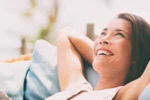 Relaxing home lifestyle happy woman in relax luxury hotel room sofa lying back with arms behind head smiling. Asian girl in comfortable lounging chair travel living.